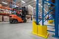 Yellow column guard installed at base of pallet rack upright in distribution center with forklift approaching